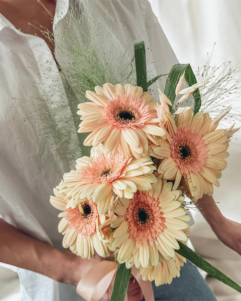Person holding a bouquet of pink and yellow flowers against a neutral background