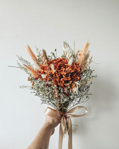 Bouquet of dried flowers with a beige ribbon held against a light background