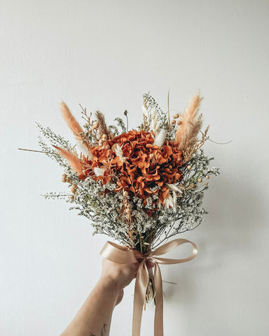 Bouquet of dried flowers with a beige ribbon held against a light background